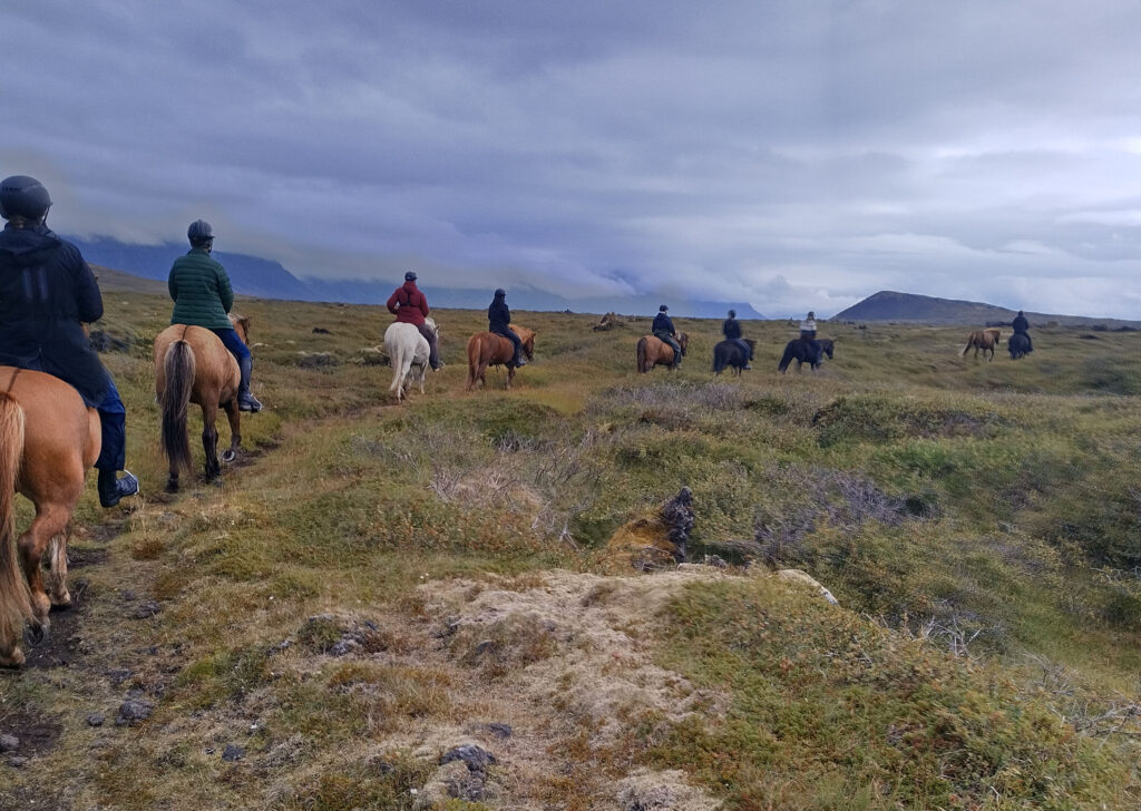 Horses and riders with the Búðaklettur volcanic cone in the background